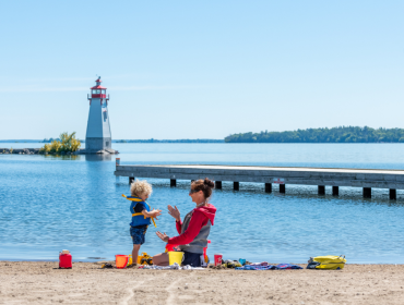 mother and child playing in the sand with a light house and a small pier in the background